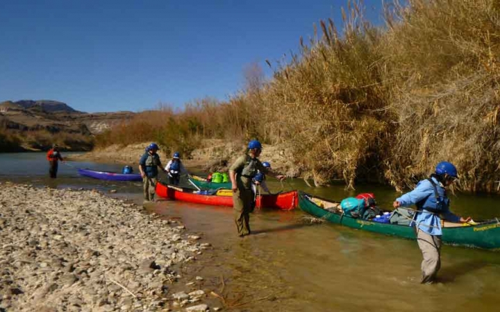 a group of gap year students guide canoes through a shallow portion of water